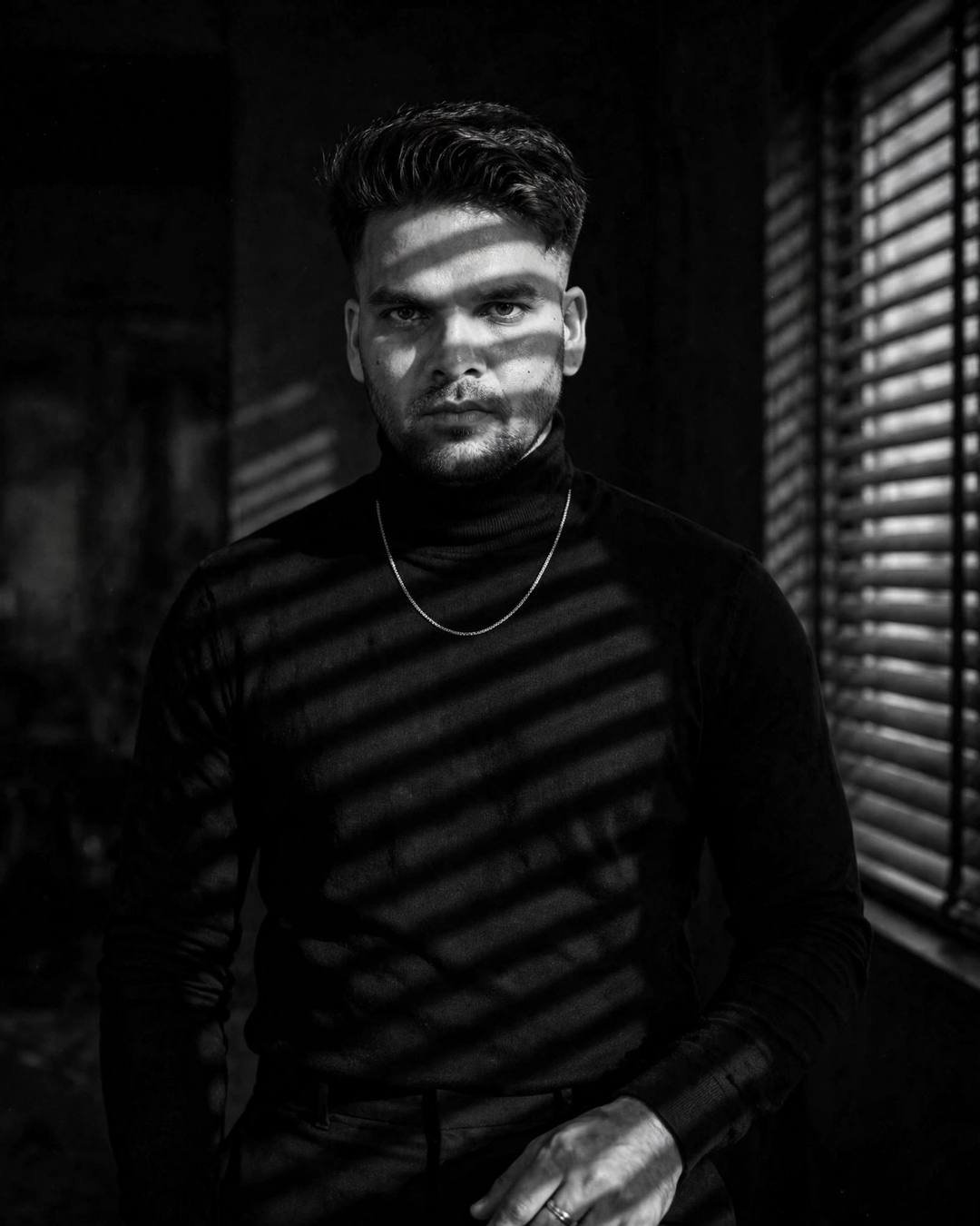 raj in a black turtleneck in a black and white noir portrait with venetian blind shadows
